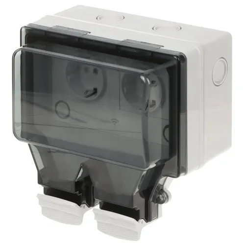 Na zdjęciu znajduje się podwójne gniazdo elektryczne z przezroczystą, ochronną pokrywą, zamontowane w szarej obudowie. Gniazdo jest przeznaczone do użytku zewnętrznego, co sugeruje jego solidna konstrukcja i zabezpieczenia przed warunkami atmosferycznymi.