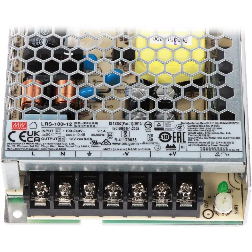 Zdjęcie przedstawia zasilacz impulsowy z metalową obudową z otworami wentylacyjnymi, ukazującą wewnętrzne komponenty elektroniczne. Na obudowie widoczne są etykiety z danymi technicznymi i certyfikatami.