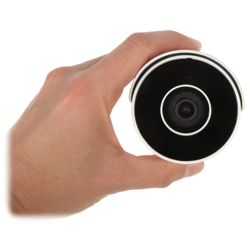 Na zdjęciu widać rękę trzymającą okrągłą kamerę monitoringu z czarnym frontem i centralnie umieszczonym obiektywem. Kamera ma biały korpus i jest widoczna na białym tle.