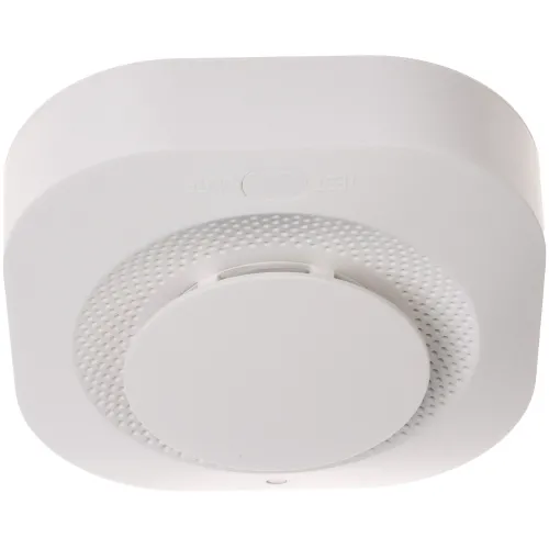 Bezprzewodowa czujka dymu w białej obudowie z centralnym przyciskiem testowym. Urządzenie ma kwadratowy kształt z zaokrąglonymi rogami i perforowaną powierzchnię wokół przycisku.