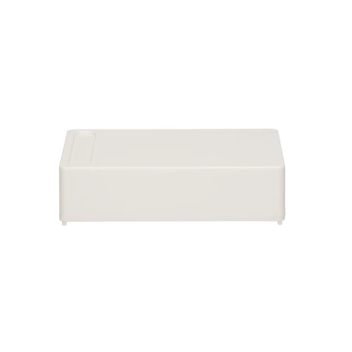 Prostokątne, białe pudełko z zaokrąglonymi krawędziami i niewielkimi nóżkami na spodzie. Na górnej powierzchni znajduje się delikatne wgłębienie w jednym z rogów.