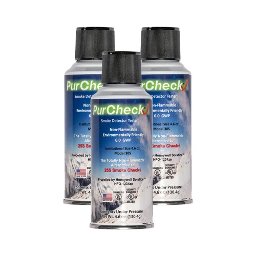Trzy puszki gazu testowego do czujek dymu marki PurCheck ustawione są na białym tle. Każda puszka ma etykietę z informacjami o produkcie, w tym o jego niepalności i przyjazności dla środowiska.