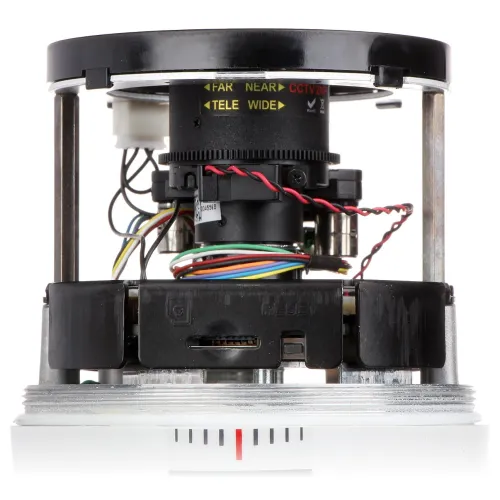 Zdjęcie przedstawia zbliżenie na mechanizm kamery z widocznymi kolorowymi przewodami, gniazdem na kartę pamięci oraz przyciskiem reset. W górnej części widoczne są oznaczenia dotyczące ustawień ostrości i zoomu.