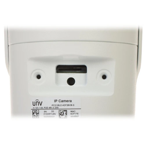 Zdjęcie przedstawia zbliżenie na gniazdo karty pamięci oraz przycisk reset na białej obudowie kamery IP. Widoczne są również etykiety z informacjami technicznymi i numerami seryjnymi urządzenia.