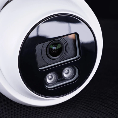 Zbliżenie na białą, kopułową kamerę IP z czarnym panelem frontowym, na którym znajduje się obiektyw oraz dwa diody LED. Kamera jest umieszczona na ciemnym tle, co podkreśla jej nowoczesny design.