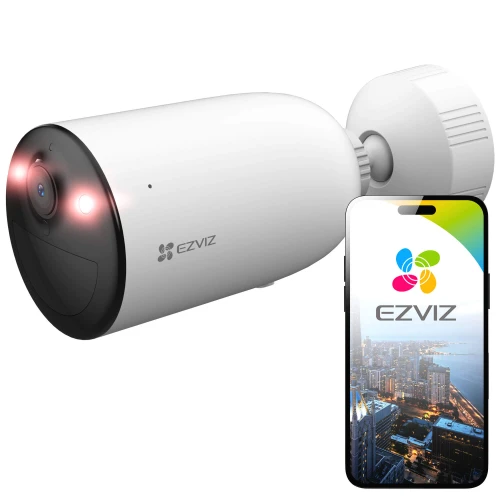 Na zdjęciu znajduje się biała kamera bezpieczeństwa EZVIZ z akumulatorem, obok której widoczny jest smartfon z aplikacją EZVIZ pokazującą widok miasta. Kamera ma cylindryczny kształt i jest wyposażona w diody LED na przednim panelu.