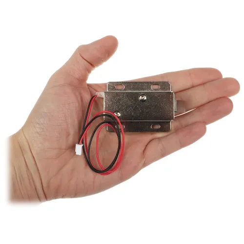 Osoba trzyma w dłoni mały, metalowy zamek elektromagnetyczny z przymocowanymi przewodami. Zamek jest prostokątny, z otworami montażowymi i widocznymi śrubami.