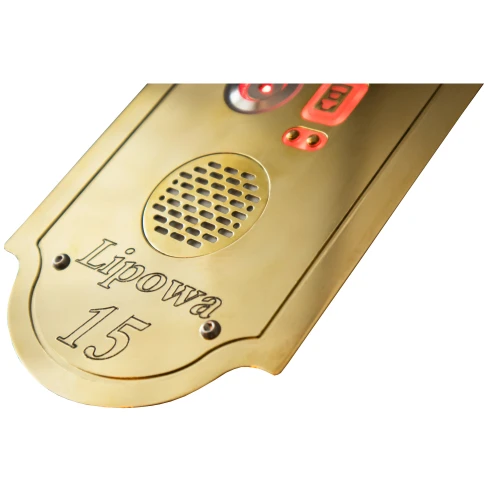 Na zdjęciu znajduje się złoty panel domofonowy z głośnikiem i podświetlanymi przyciskami. Na dole panelu wygrawerowany jest napis "Lipowa 15".