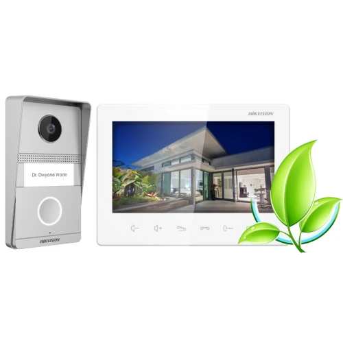 Na zdjęciu znajduje się wideodomofon Hikvision, składający się z panelu zewnętrznego z kamerą i monitora wewnętrznego wyświetlającego obraz nowoczesnego domu. Obok urządzenia widoczna jest grafika przedstawiająca zielony liść.