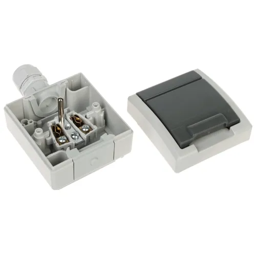 Zdjęcie przedstawia otwartą obudowę elektryczną z widocznymi elementami montażowymi i przewodami wewnątrz. Obok znajduje się zdejmowana pokrywa w kolorze szarym z ciemniejszym panelem.