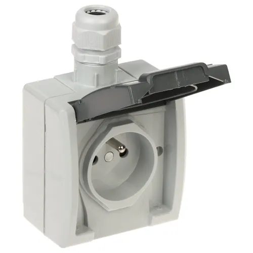 Na zdjęciu znajduje się szara, pojedyncza gniazdko elektryczne z klapką ochronną, przeznaczone do montażu natynkowego. Gniazdko posiada dodatkowy dławik kablowy na górze obudowy.