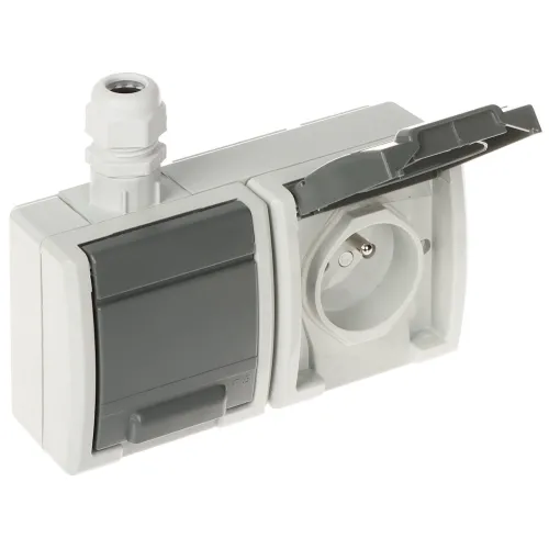 Na zdjęciu znajduje się podwójne gniazdo elektryczne z szarymi klapkami ochronnymi, jedno z nich jest otwarte, ukazując wnętrze gniazda. Obudowa gniazda jest w kolorze jasnoszarym, a na górze znajduje się przepust kablowy.