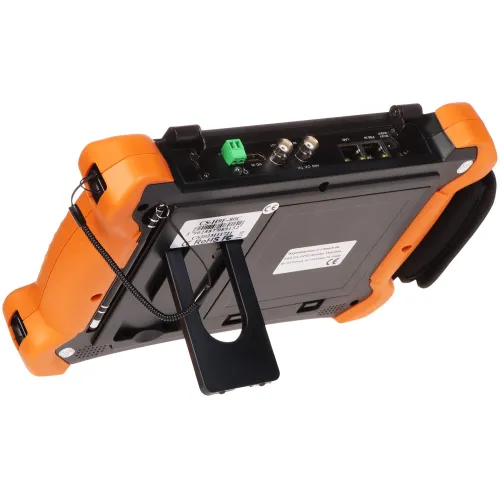 Na zdjęciu widoczny jest tył przenośnego urządzenia elektronicznego z pomarańczową obudową ochronną i czarną podpórką. Urządzenie posiada różne porty i złącza na górnej krawędzi.