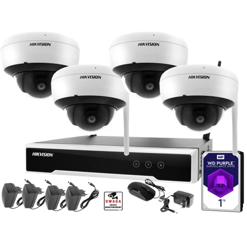Zestaw monitoringu składający się z czterech kamer kopułkowych Hikvision, rejestratora, dysku twardego WD Purple 1TB oraz akcesoriów takich jak zasilacze i myszka. Na zdjęciu widoczne są również naklejki ostrzegawcze dotyczące monitoringu.
